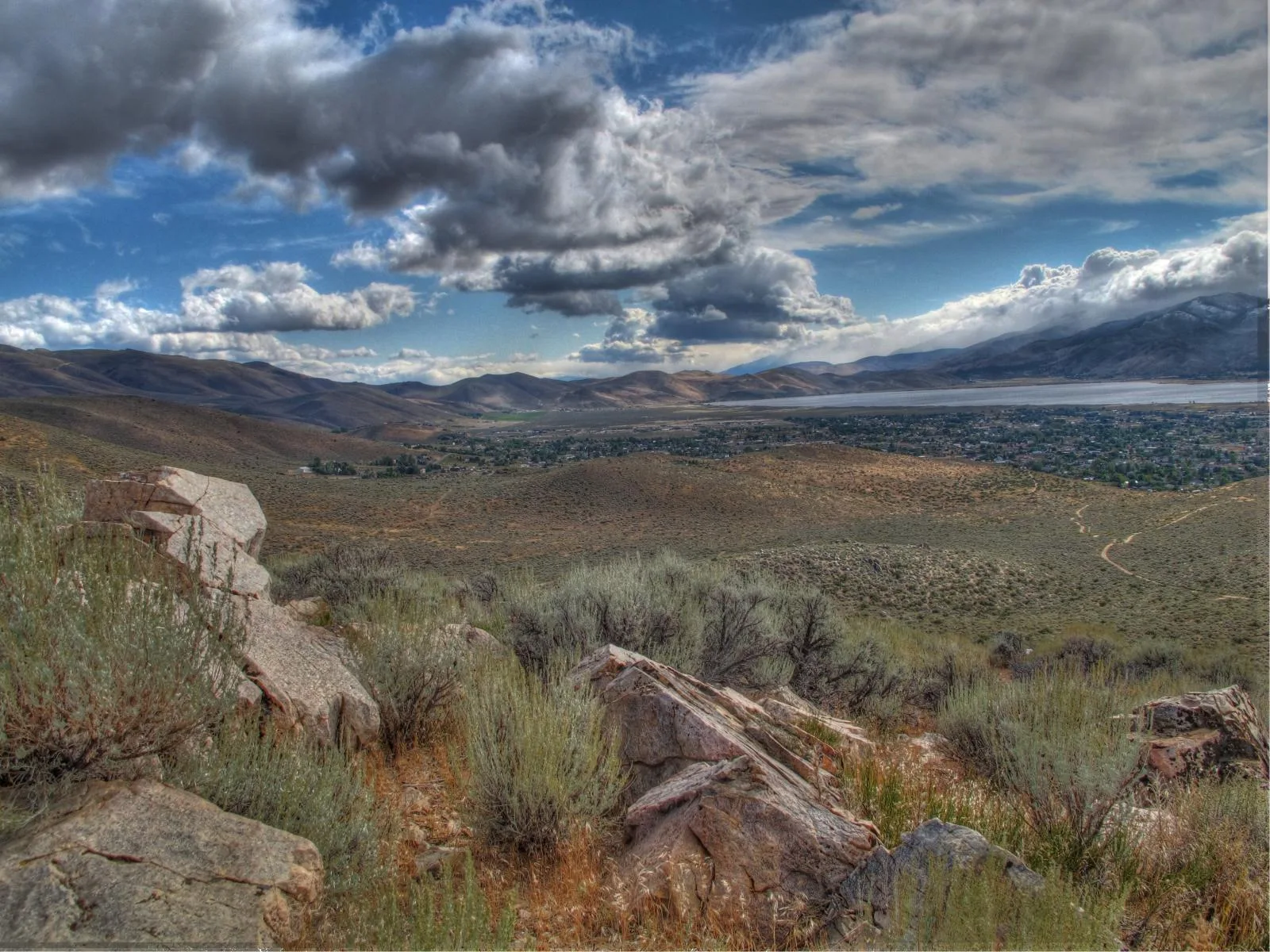 Rocky sagebrush hillside looking over a valley and lake under storm clouds