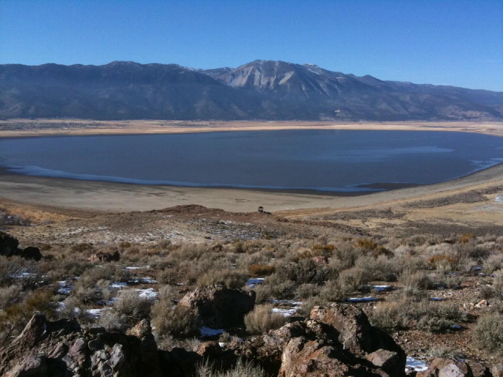 Wide lake below a rocky hillside with the Carson Range in the background