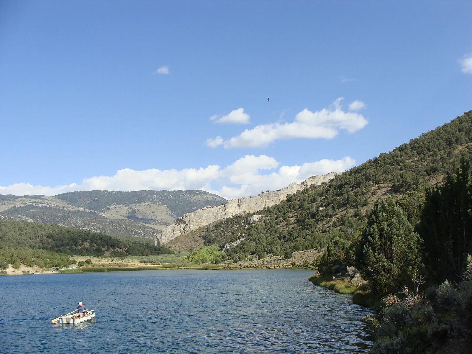 Blue reservoir with a small boat below forested hills and a rocky ridge