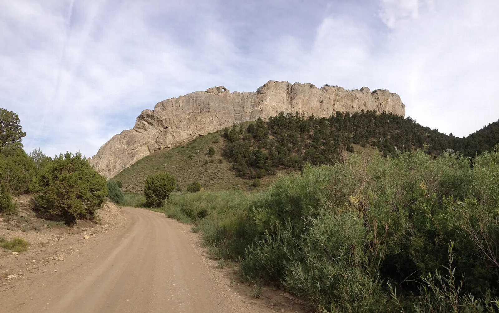 Dirt road leading toward a tall rock wall above a brushy hillside