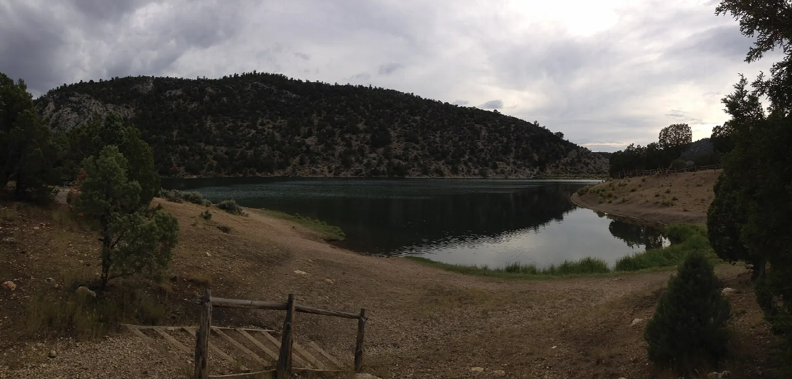 Dark reservoir seen past a wooden fence with forested hills behind