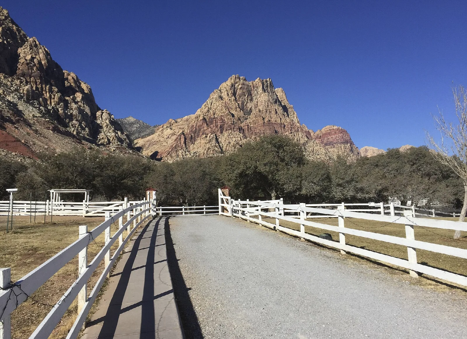 White ranch fence along a gravel path with red rock mountains behind