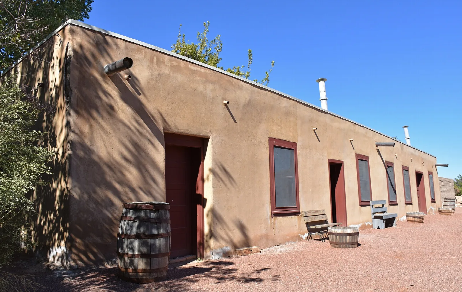 Long adobe building with red doors and a barrel out front
