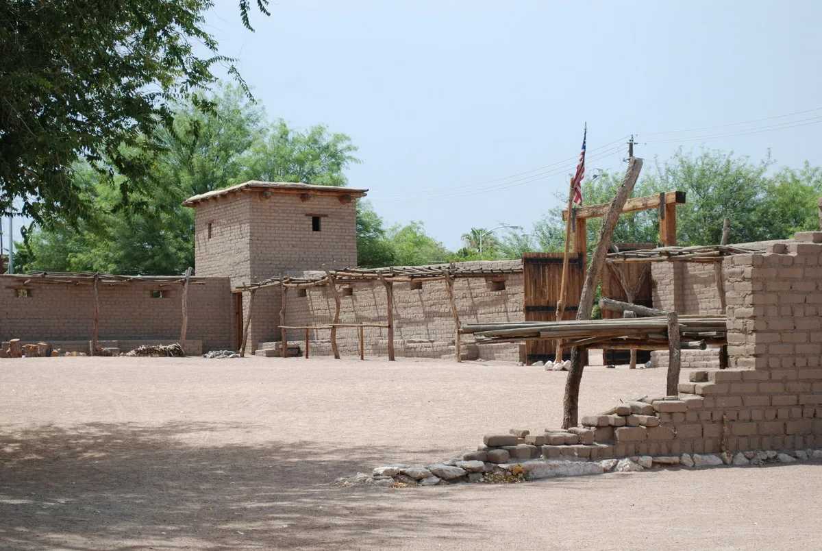 Adobe fort walls and a small tower around a dirt yard with trees