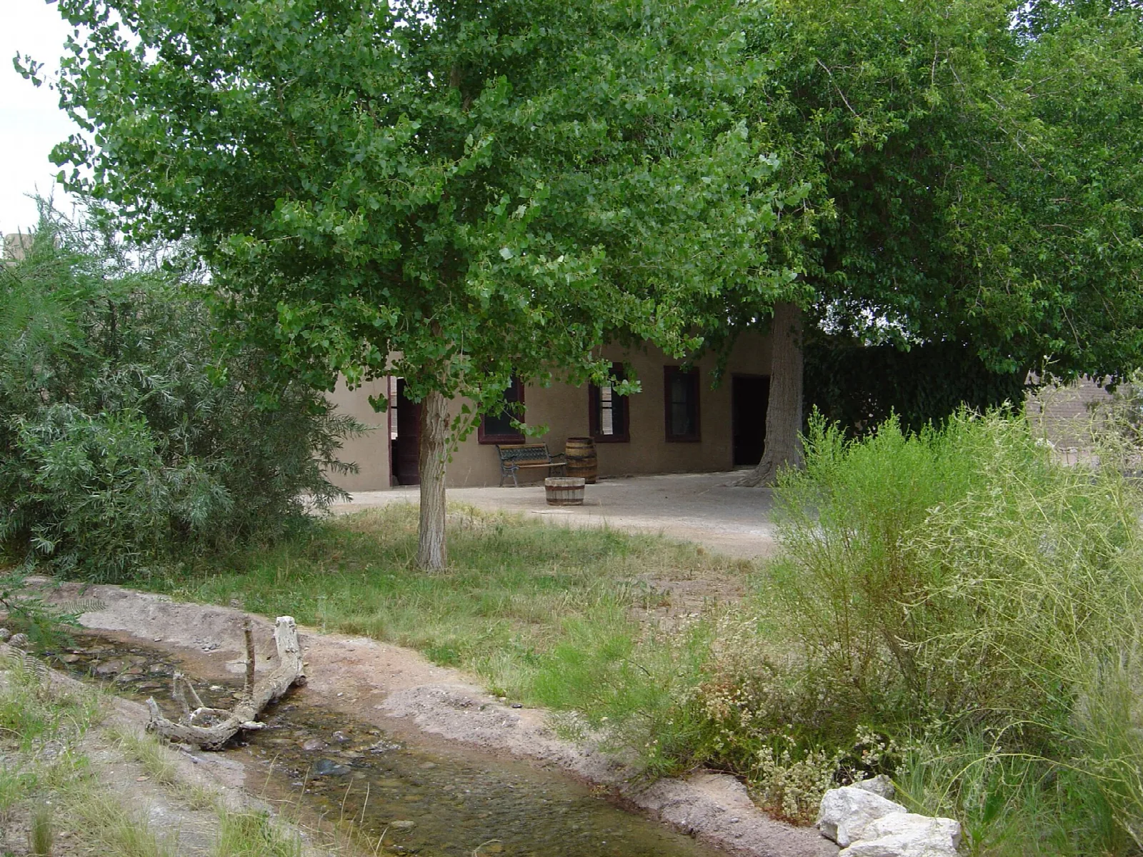 Small creek and green trees beside a low adobe building