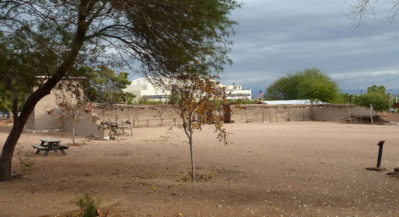 Dirt yard with a tree and picnic table beside adobe walls
