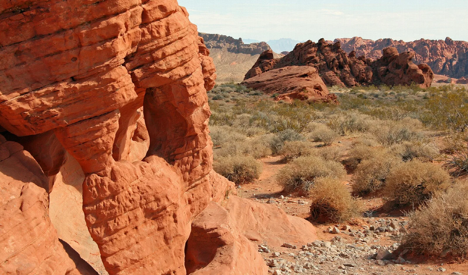 Orange sandstone rock in the foreground with desert shrubs and rocks beyond