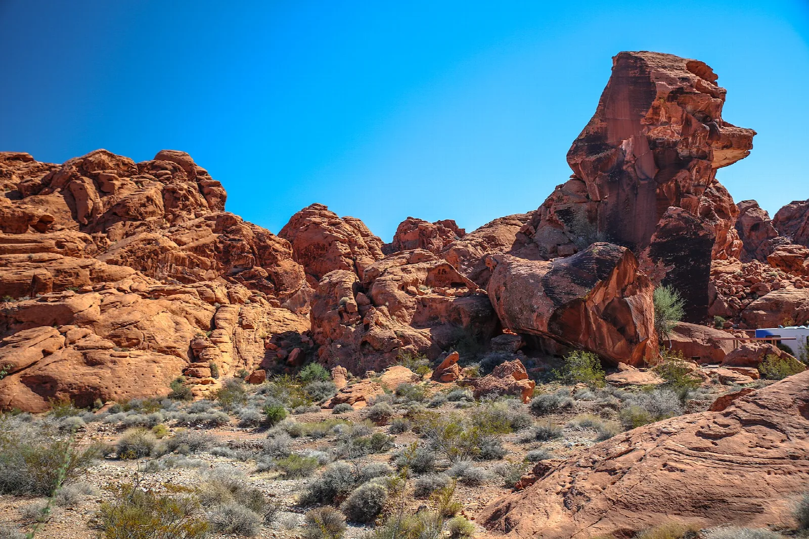 Red sandstone rock formations above desert brush under a bright blue sky