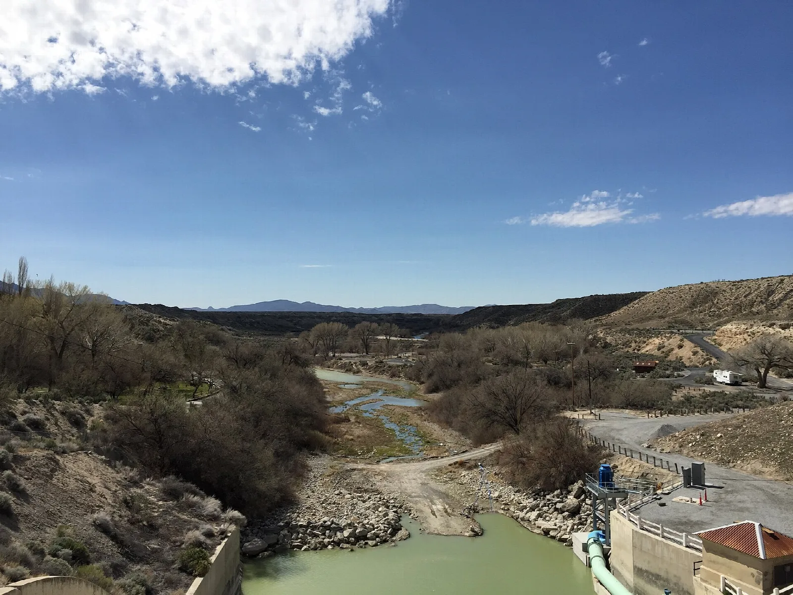 River channel below a dam with brush and rocky banks