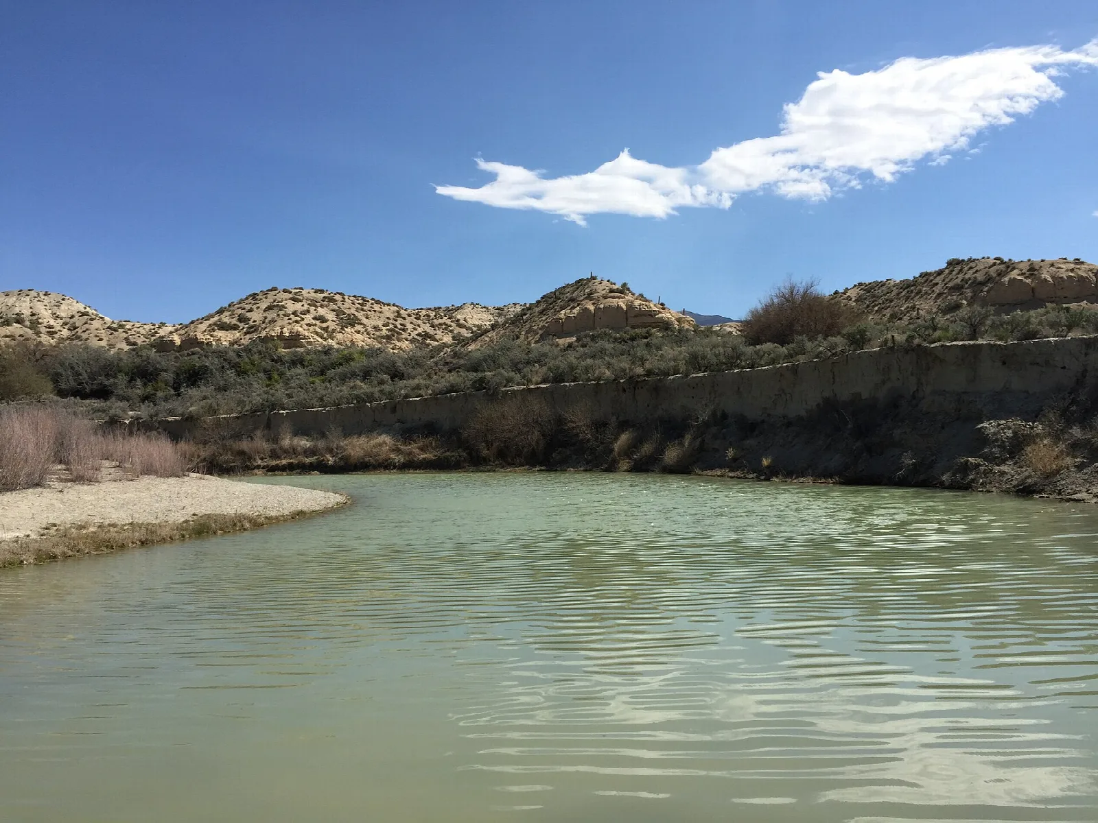 Calm green river below sandy brush-covered hills