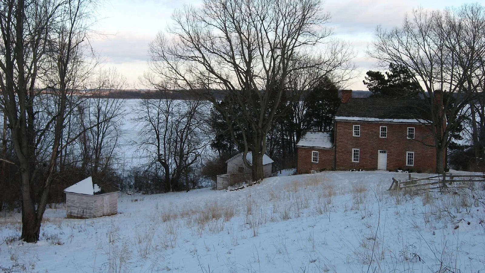 Brick farm buildings on a snowy hillside above a reservoir