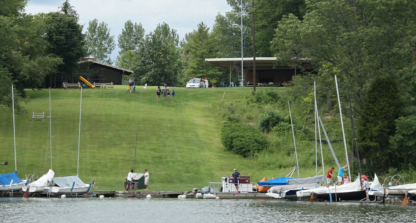 Sailboats at a dock below a grassy slope and shelter