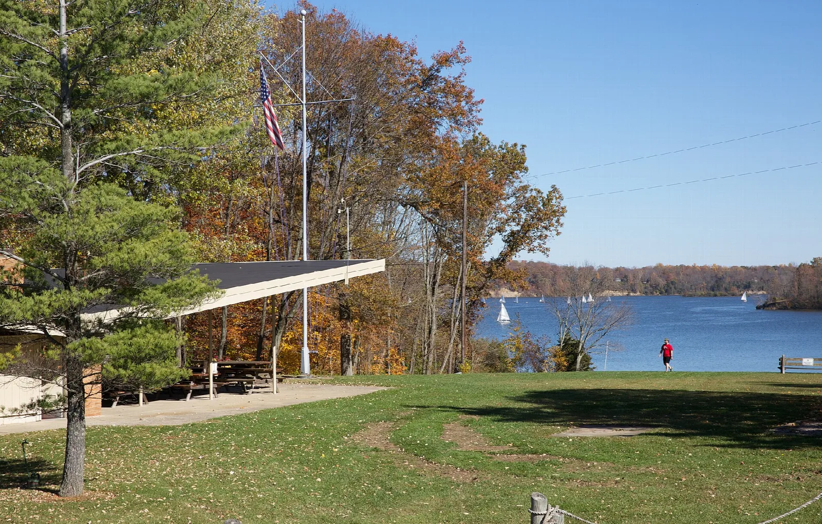 Lakeside shelter and flagpole above blue water with sailboats
