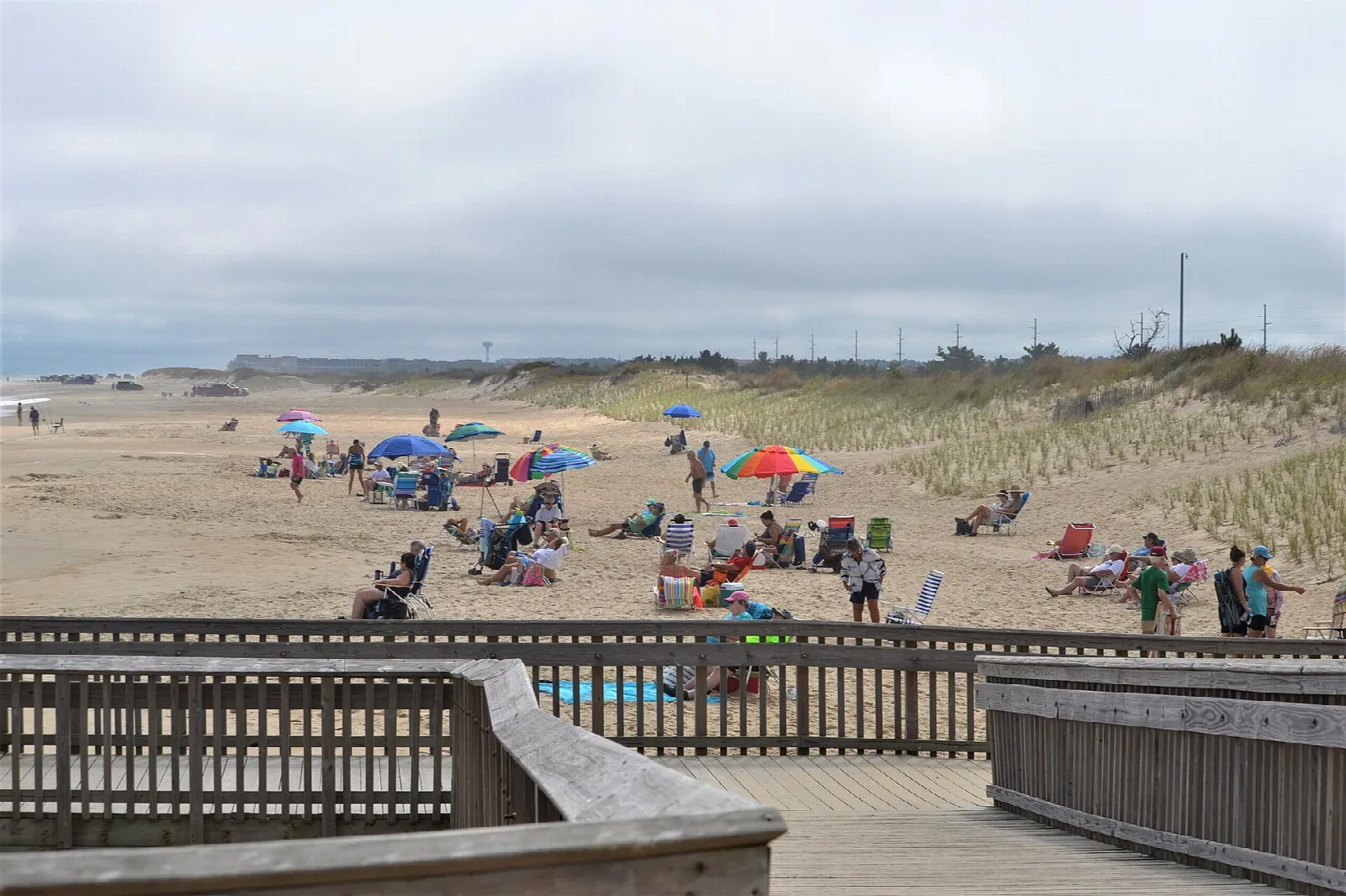 Sand beach with people and umbrellas behind a wooden boardwalk
