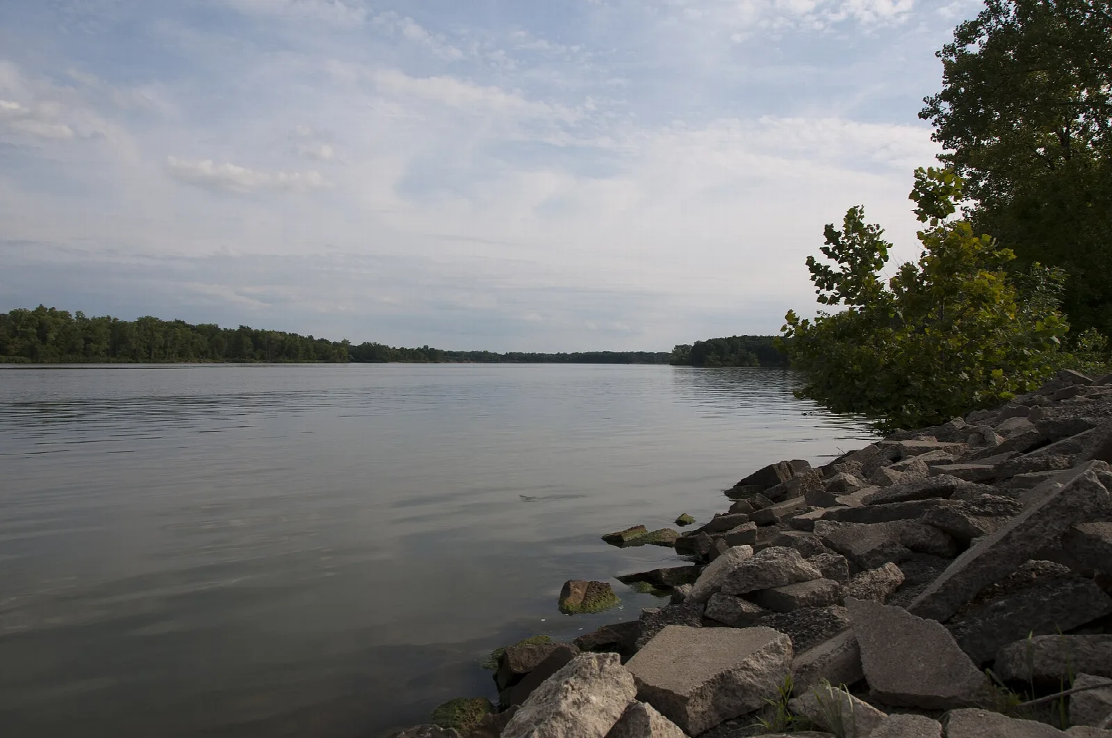 Rocky shoreline on a wide gray lake under a cloudy sky