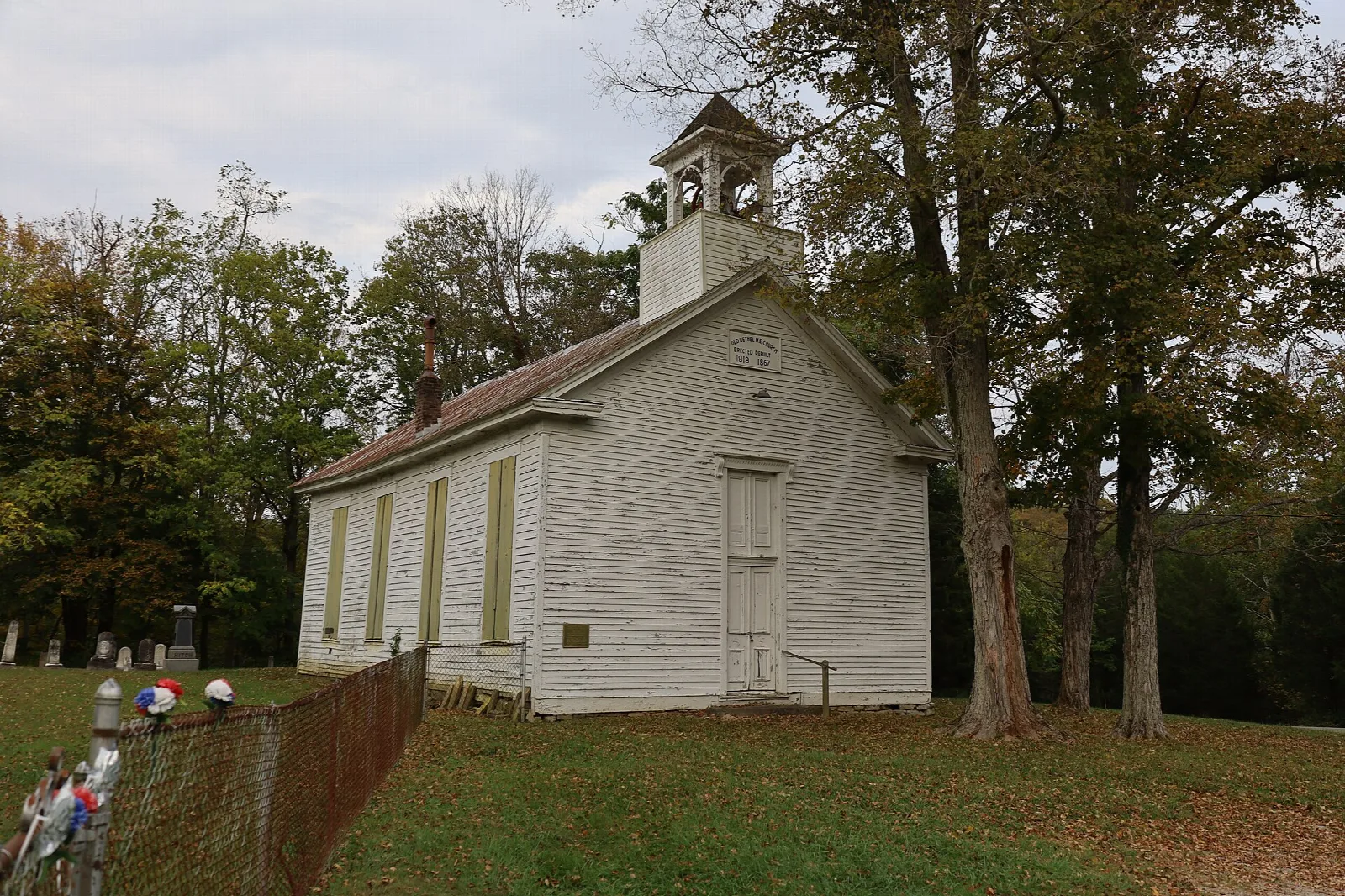 White frame church among fall trees with a cemetery beside it