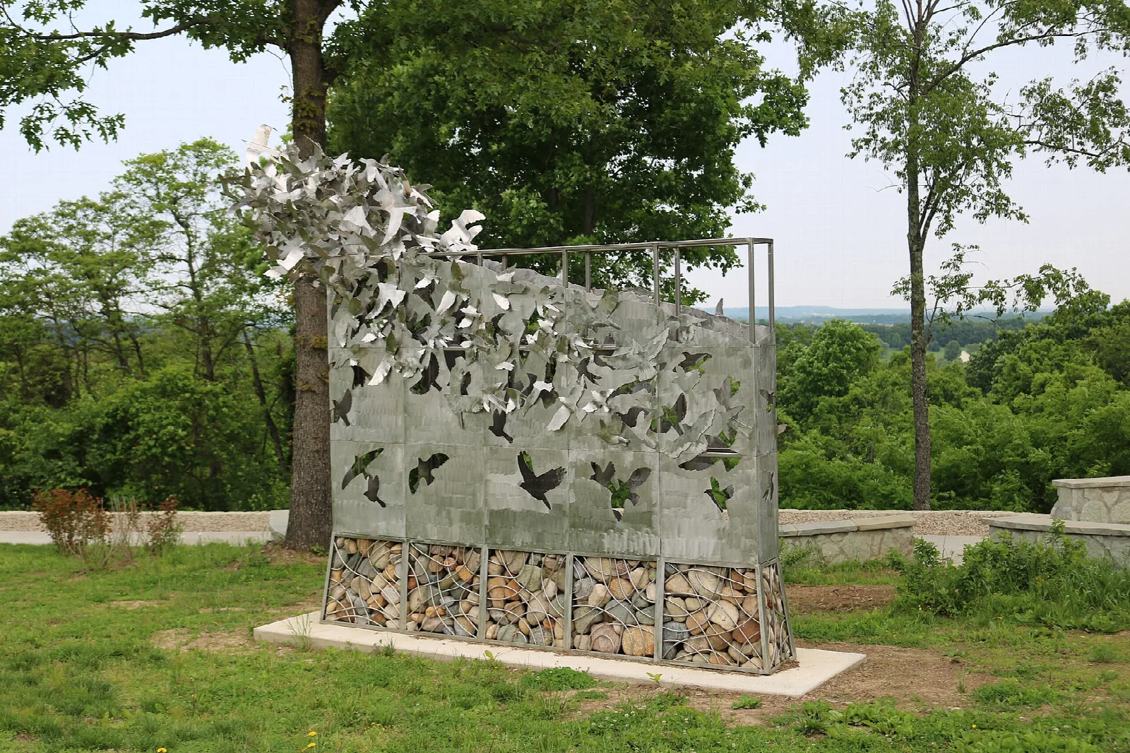 Metal sculpture with cut-out birds above a stacked stone base