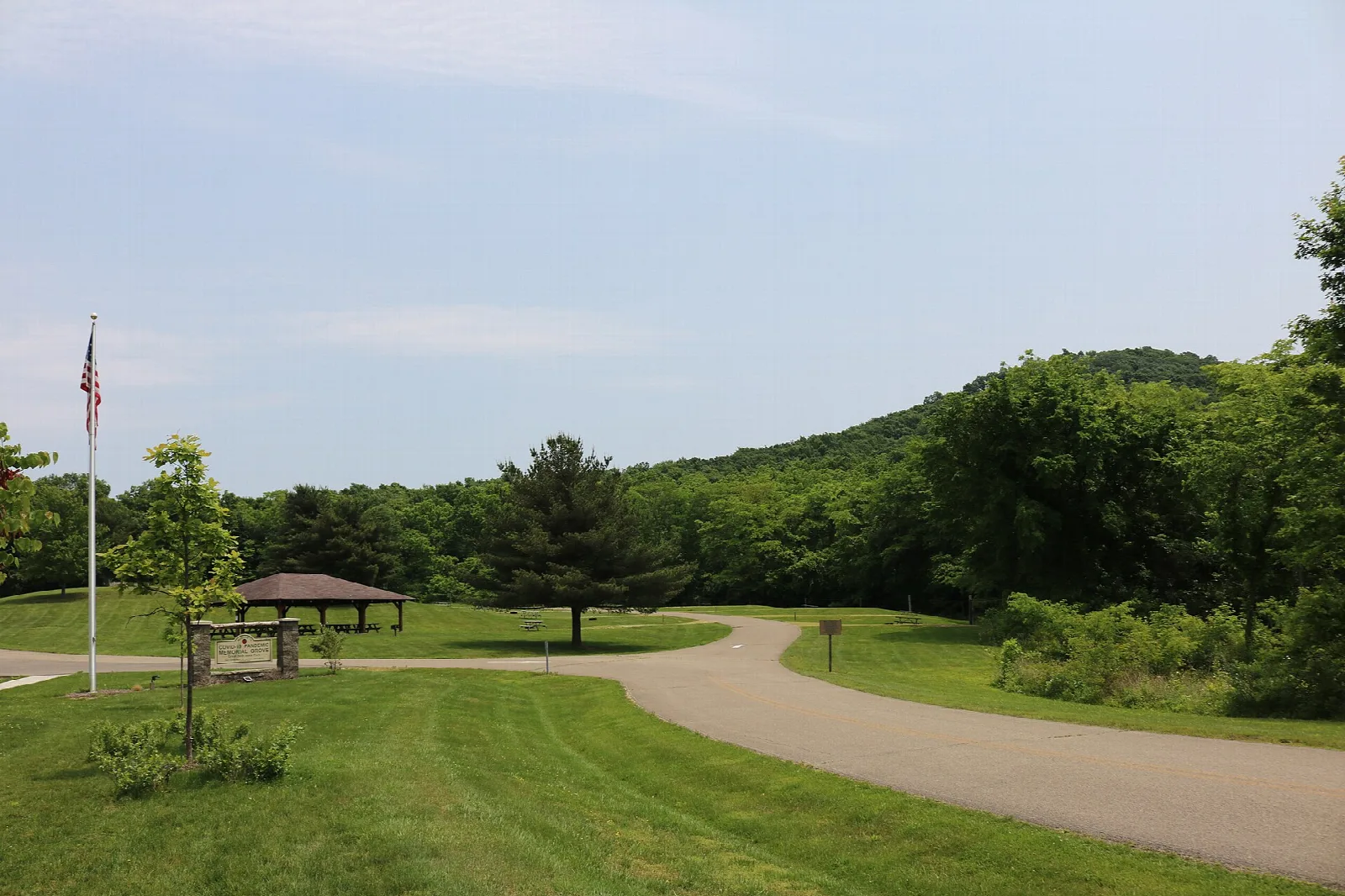 Paved path curving past a picnic shelter on a grassy hilltop