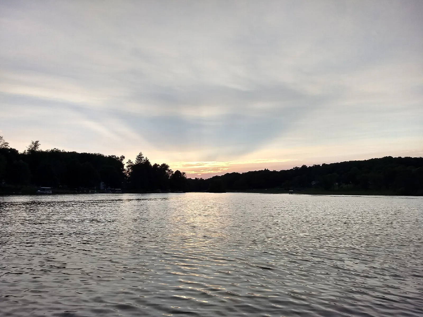 Wide lake at dusk with a dark tree line and soft clouds