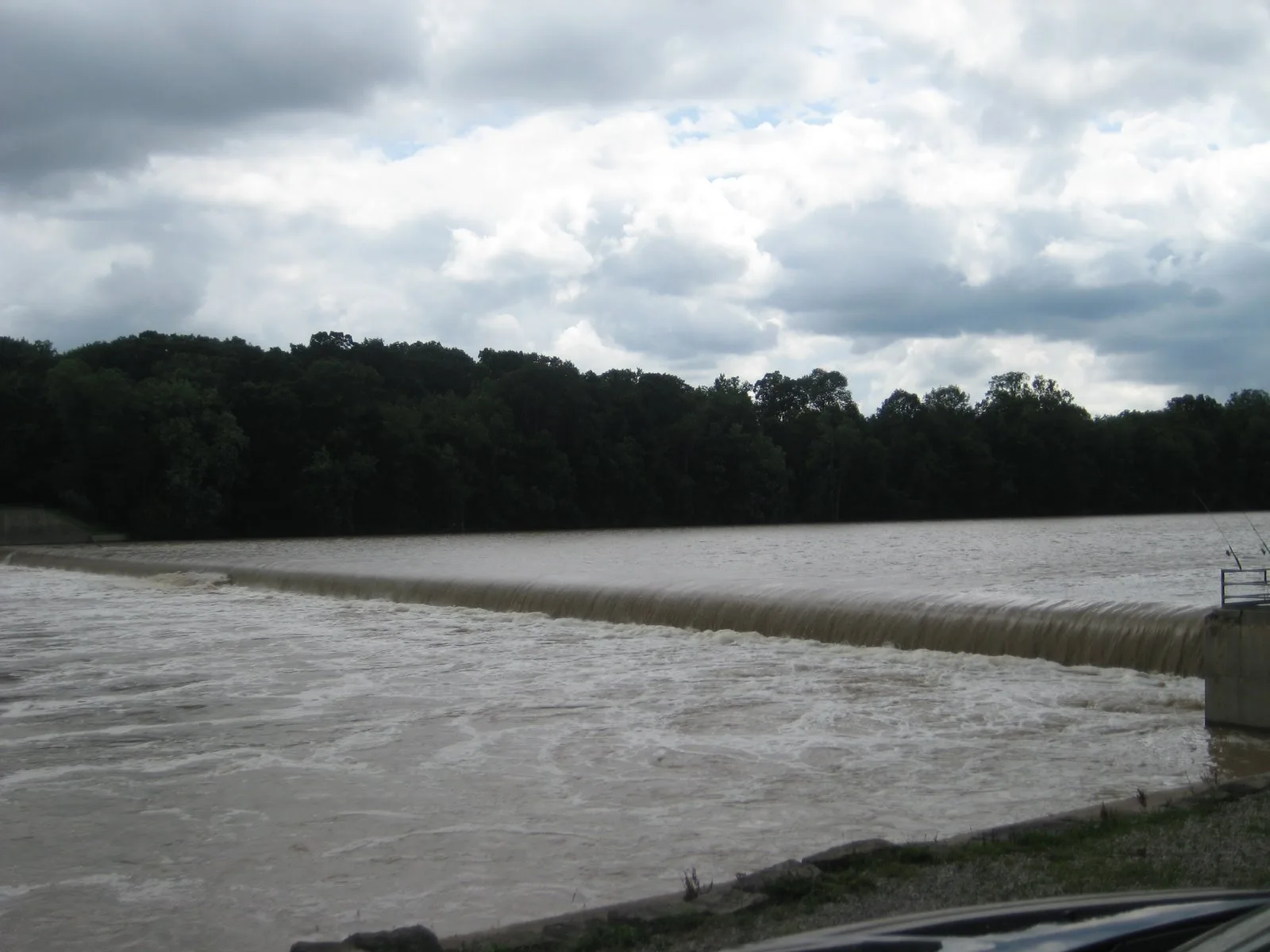 Low dam stretching across a wide brown river with forest behind