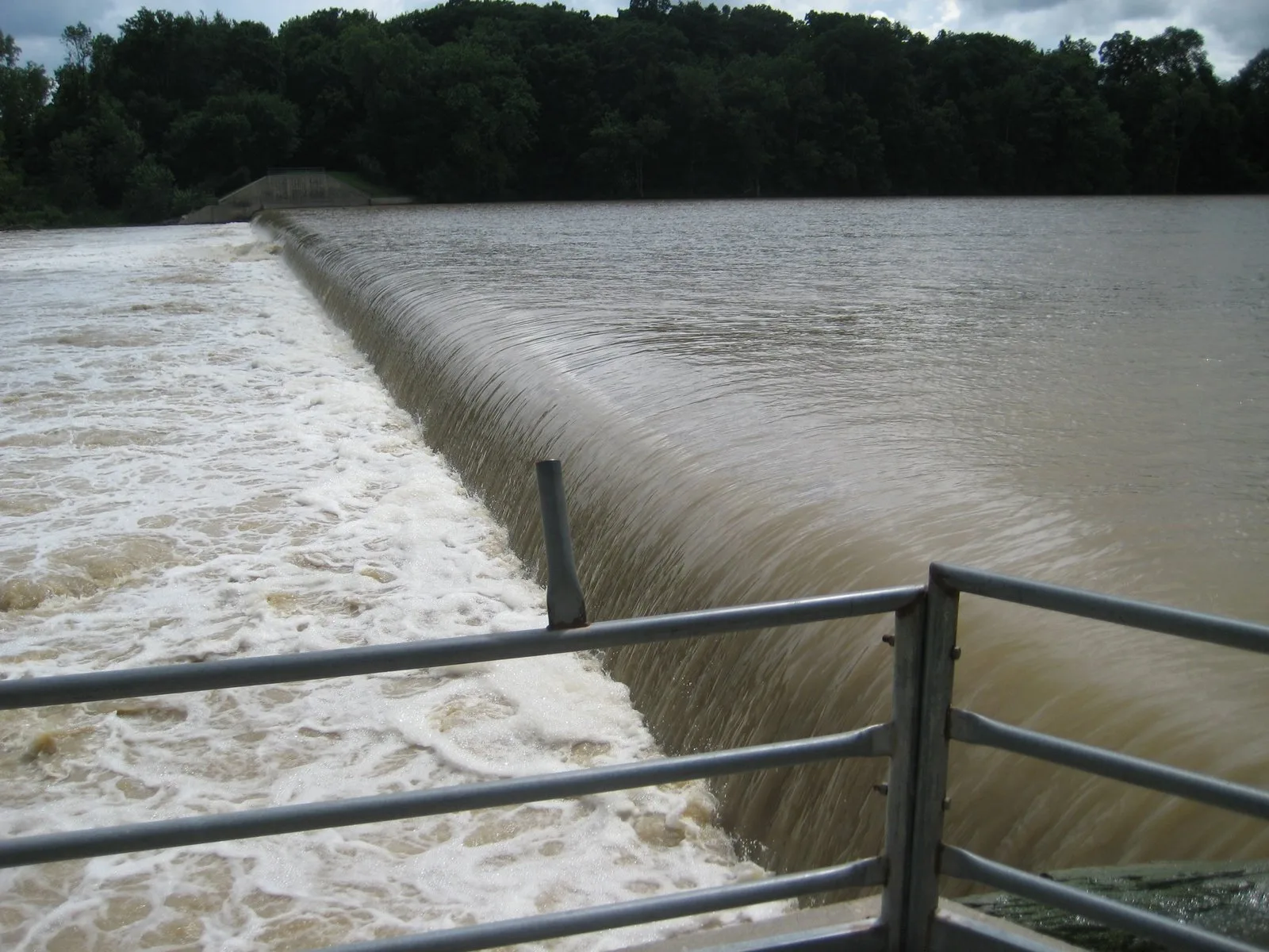 Water spilling over the dam beside a metal railing