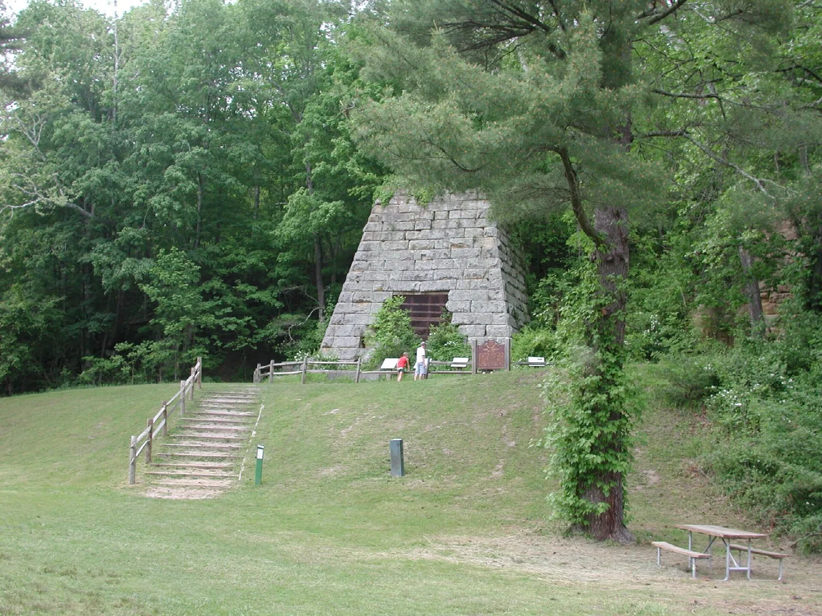 Stone iron furnace in a clearing with steps and a picnic table