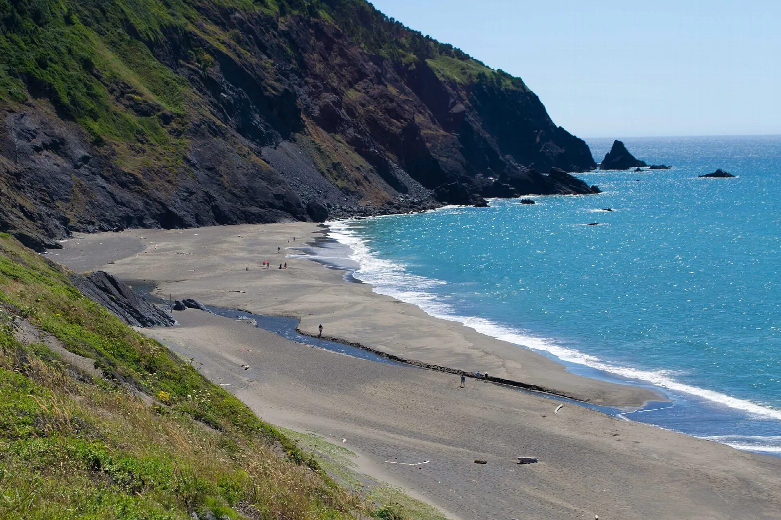 Sandy beach curving below green headland cliffs and blue water