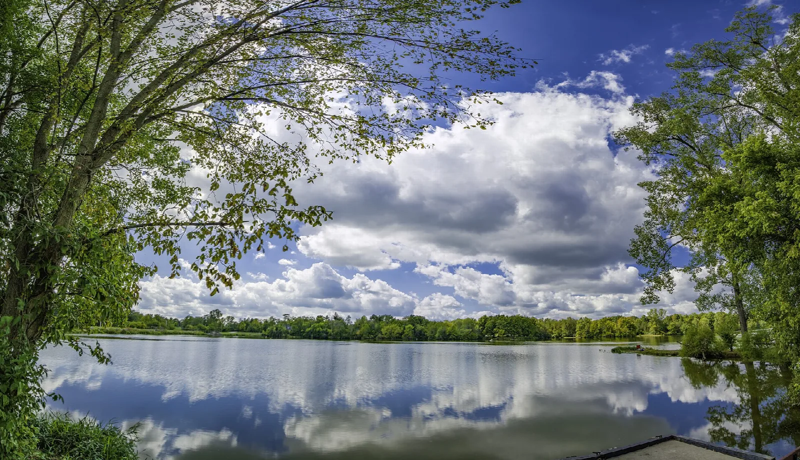 Wide lake with clouds reflected on the water, framed by trees