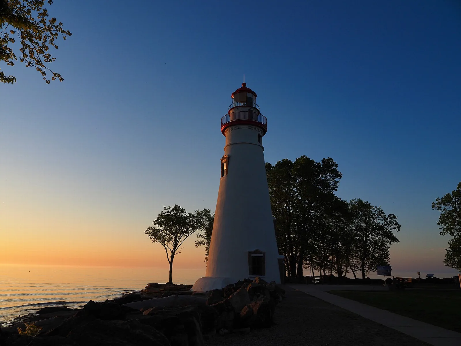 White lighthouse silhouetted by a sunset over the lake