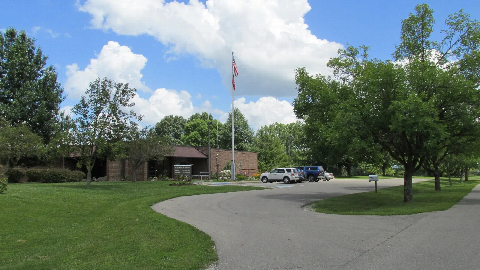 Low brick welcome center with a flagpole and a curving paved drive