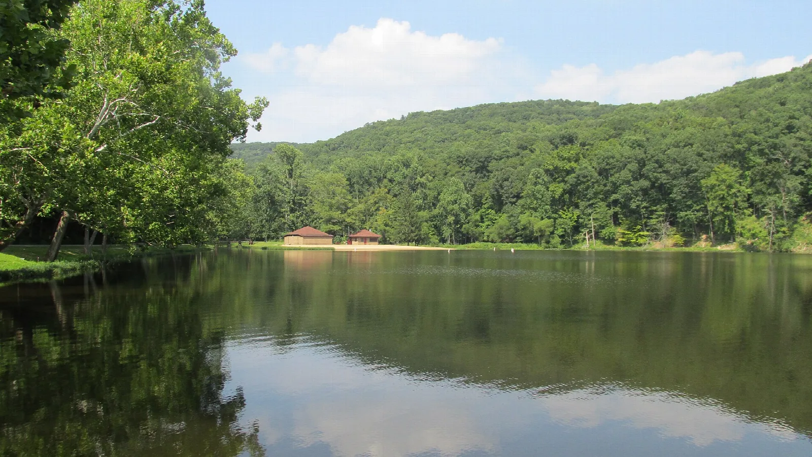 Calm lake with a forested hill rising behind and small buildings on the far shore