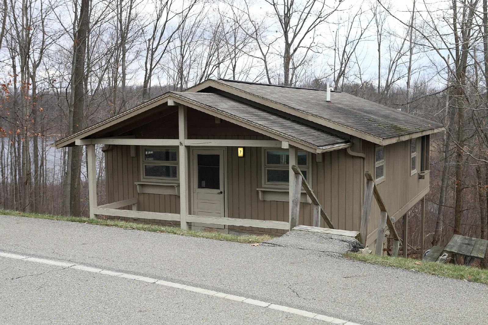 Small wooden cabin beside a paved road with bare woods