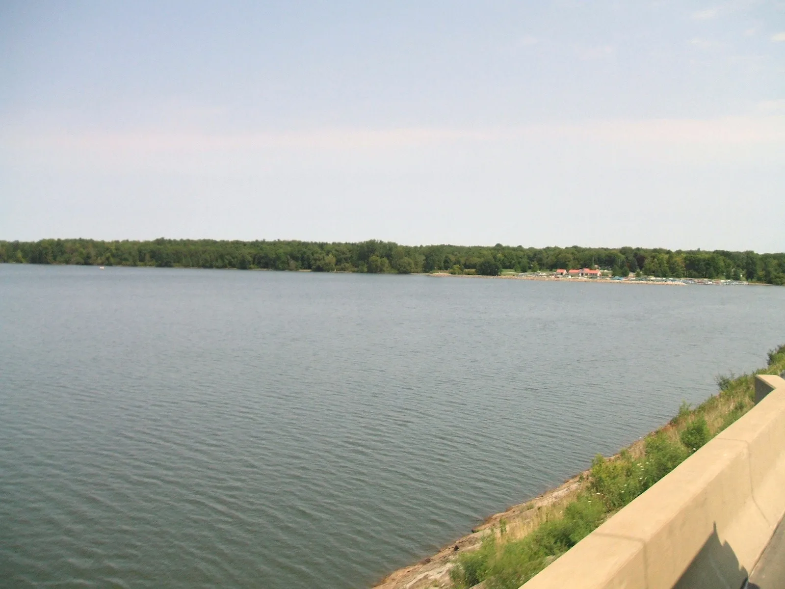 Lake and tree-lined far shore beside a concrete wall