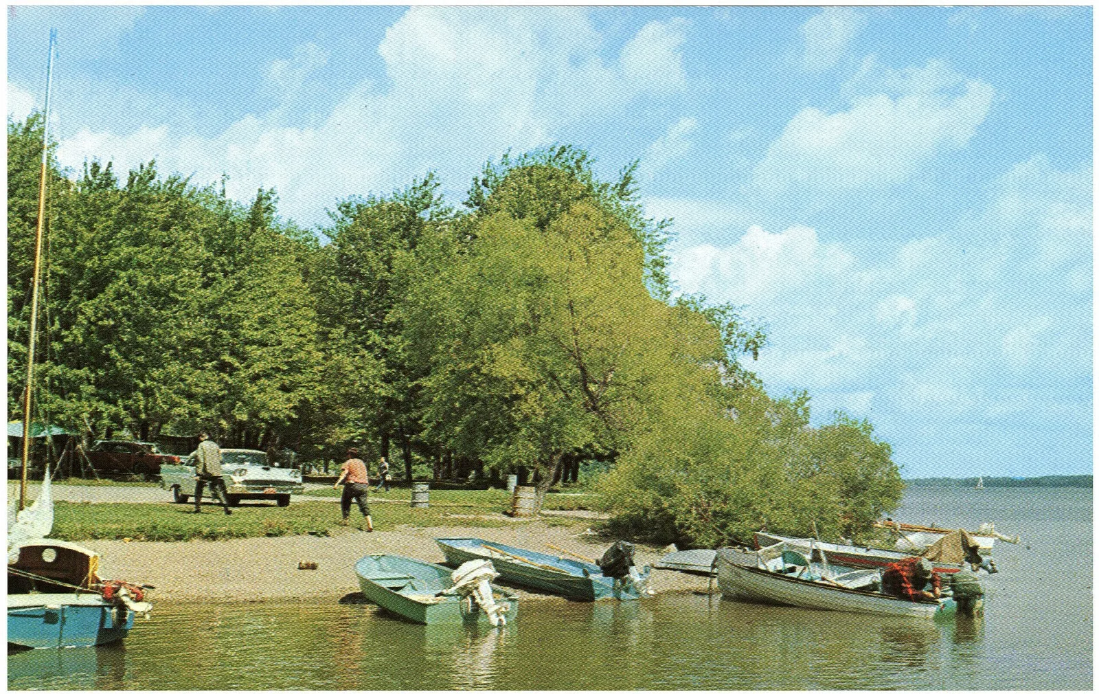 Small boats pulled up on a shaded shore with people and trees