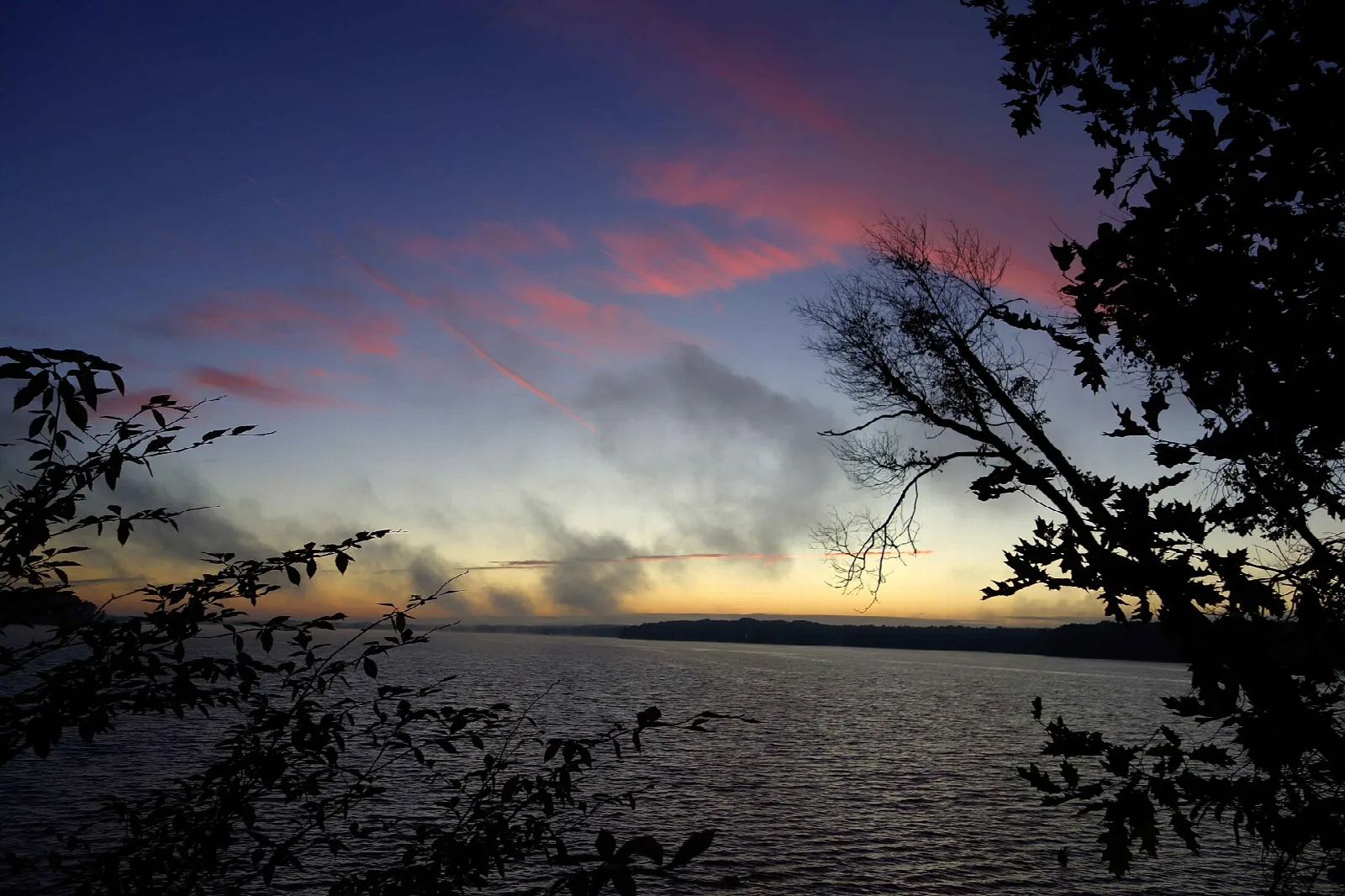 Sunrise over a lake with dark trees in the foreground