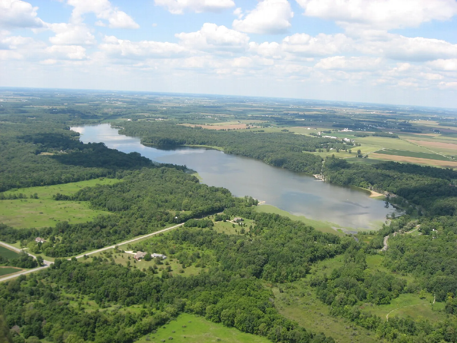 Aerial view of a long lake surrounded by forest and farm fields