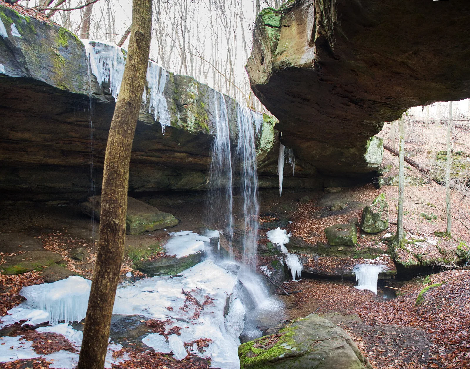 Frozen waterfall beside a rock bridge in a wooded hollow