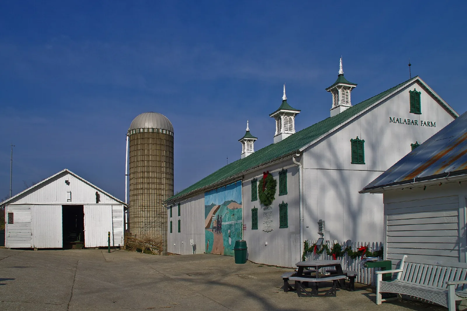 White barn with green roof and silo under a blue sky