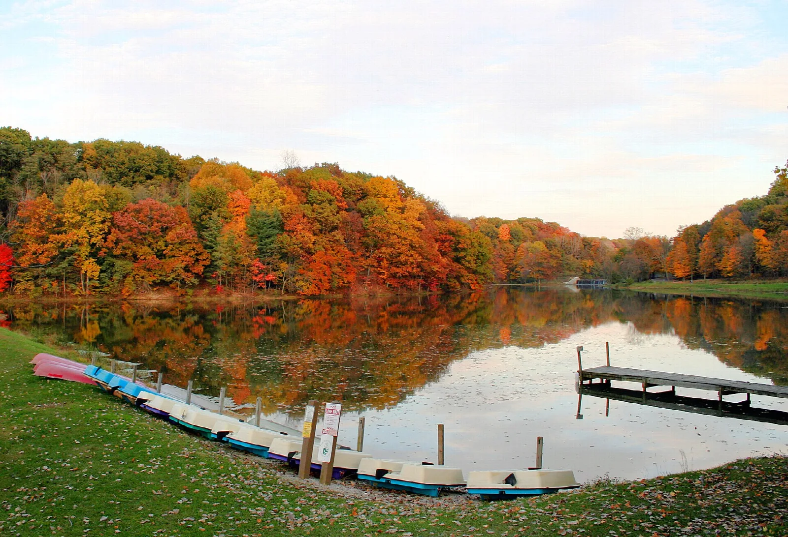 Fall-colored trees reflected in a lake beside a dock and small boats