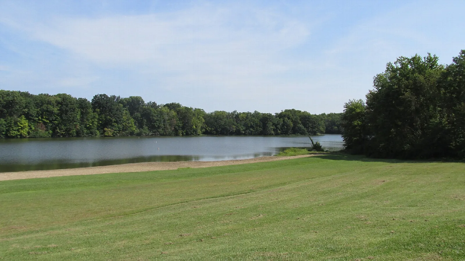 Wide mown lawn and sandy shore beside a calm lake with forest on the far side