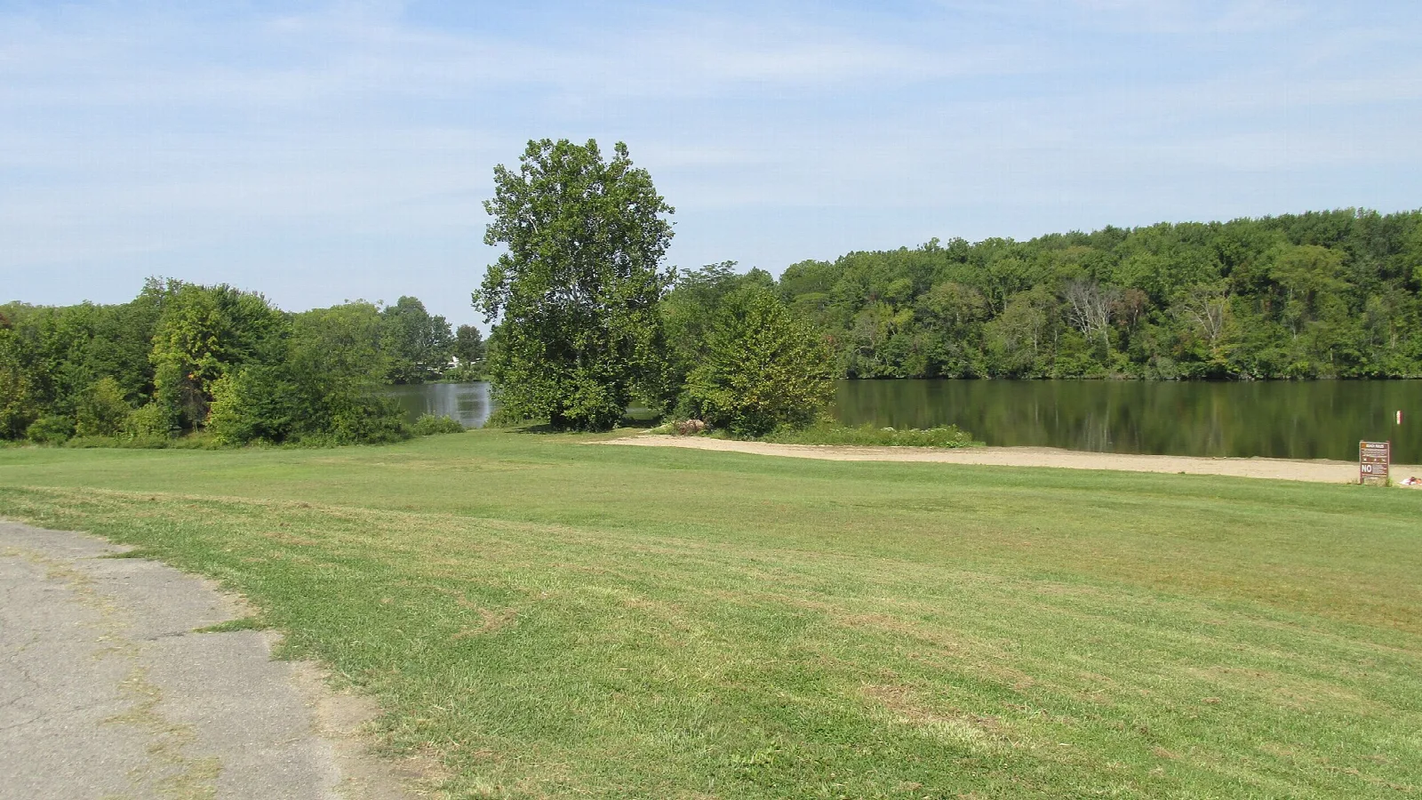 Paved path and grass leading to a lake edge ringed with trees