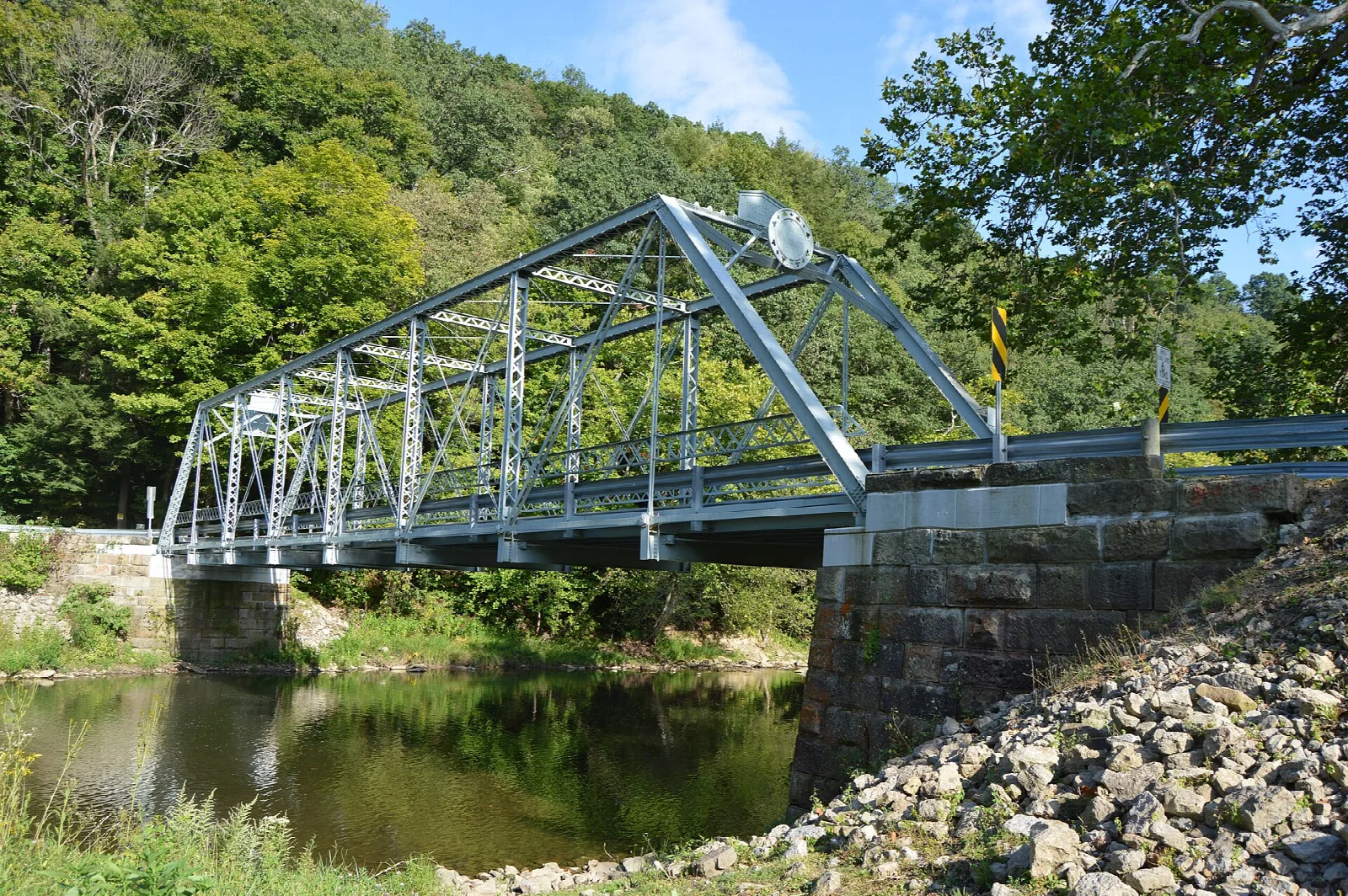 Steel truss bridge and stone abutment over still water