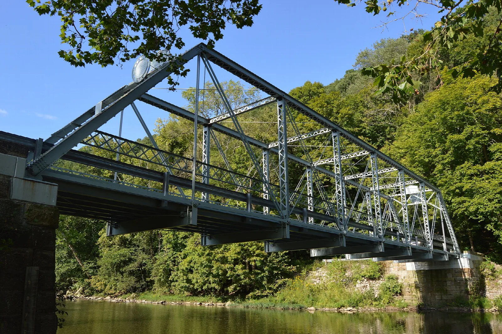 Steel truss bridge over a creek with wooded hills beyond