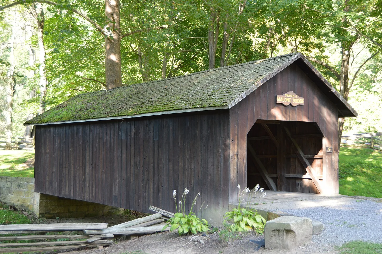 Dark wooden covered bridge with a mossy roof among trees