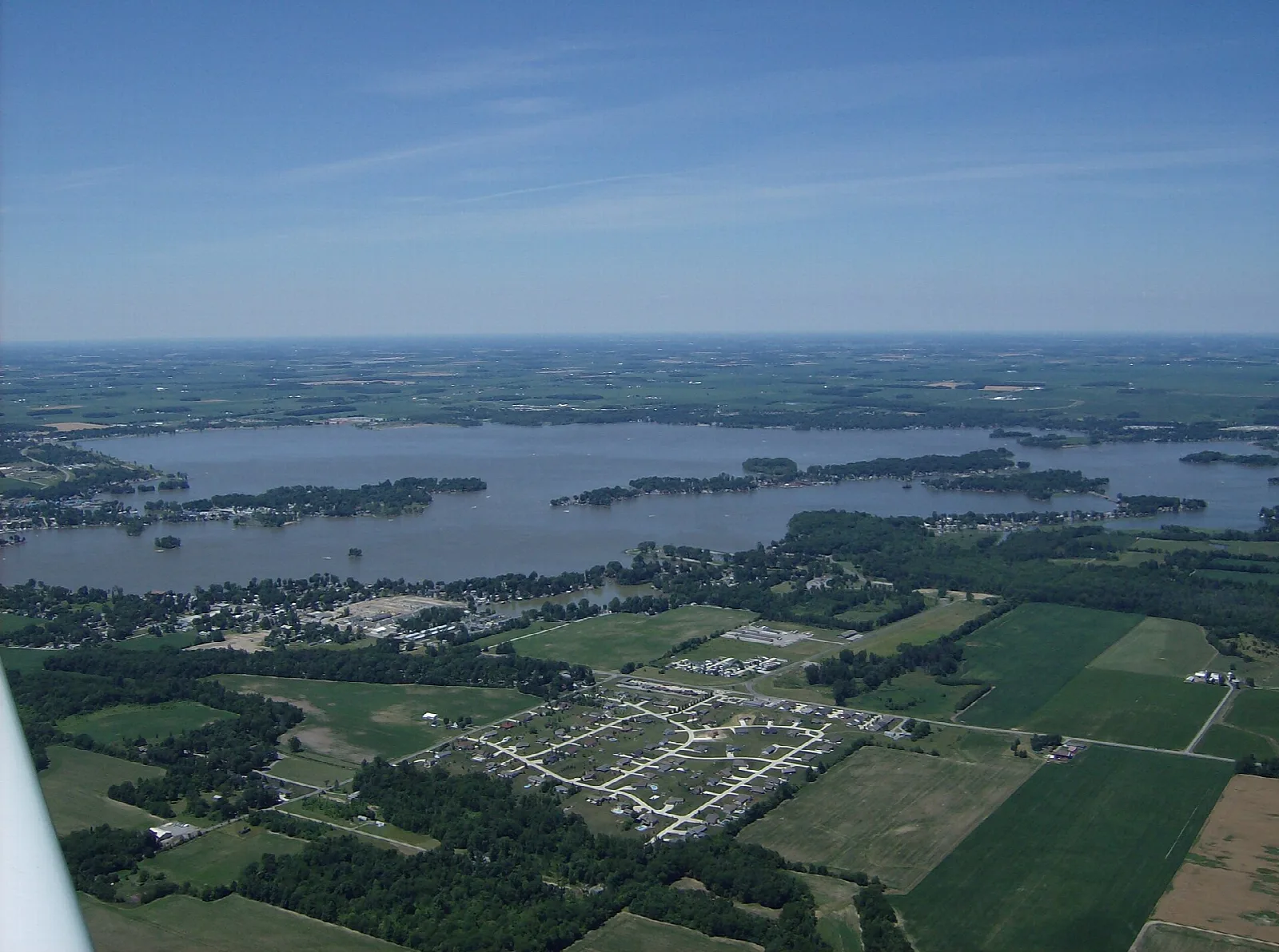 Aerial view of a wide lake with wooded islands and farm fields beside it
