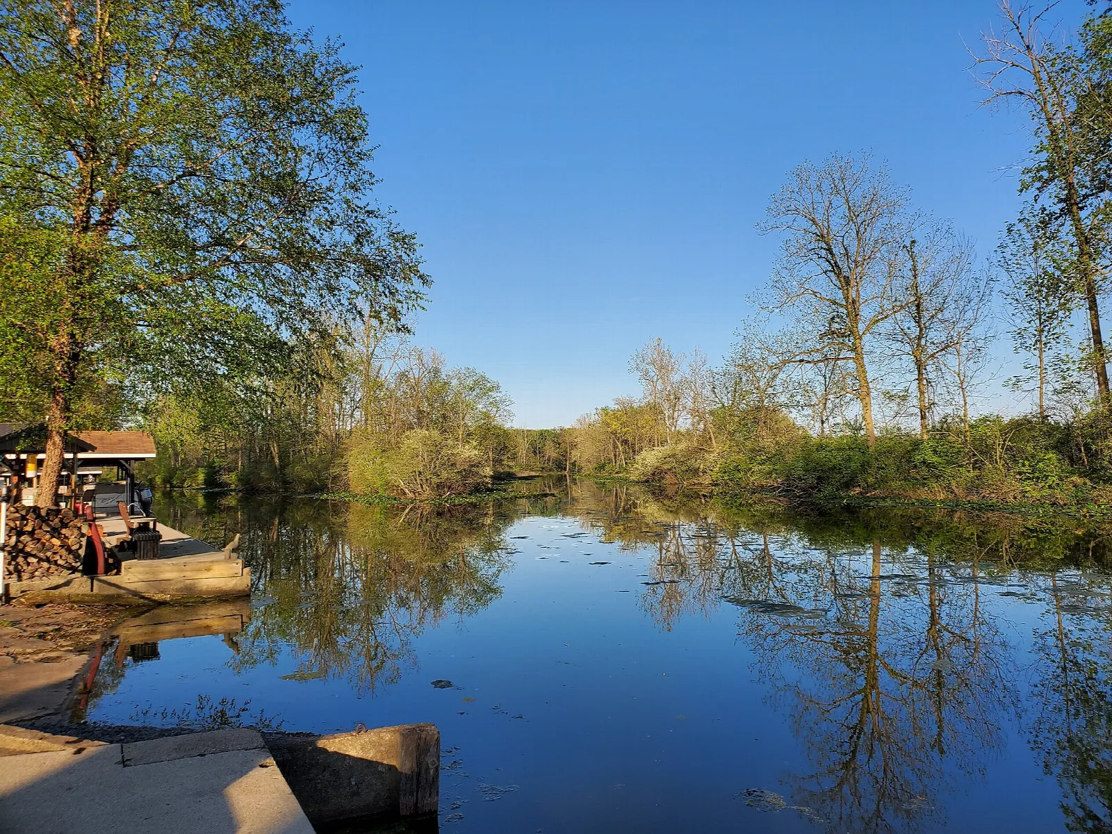 Calm blue channel with trees along the bank and a dock at left