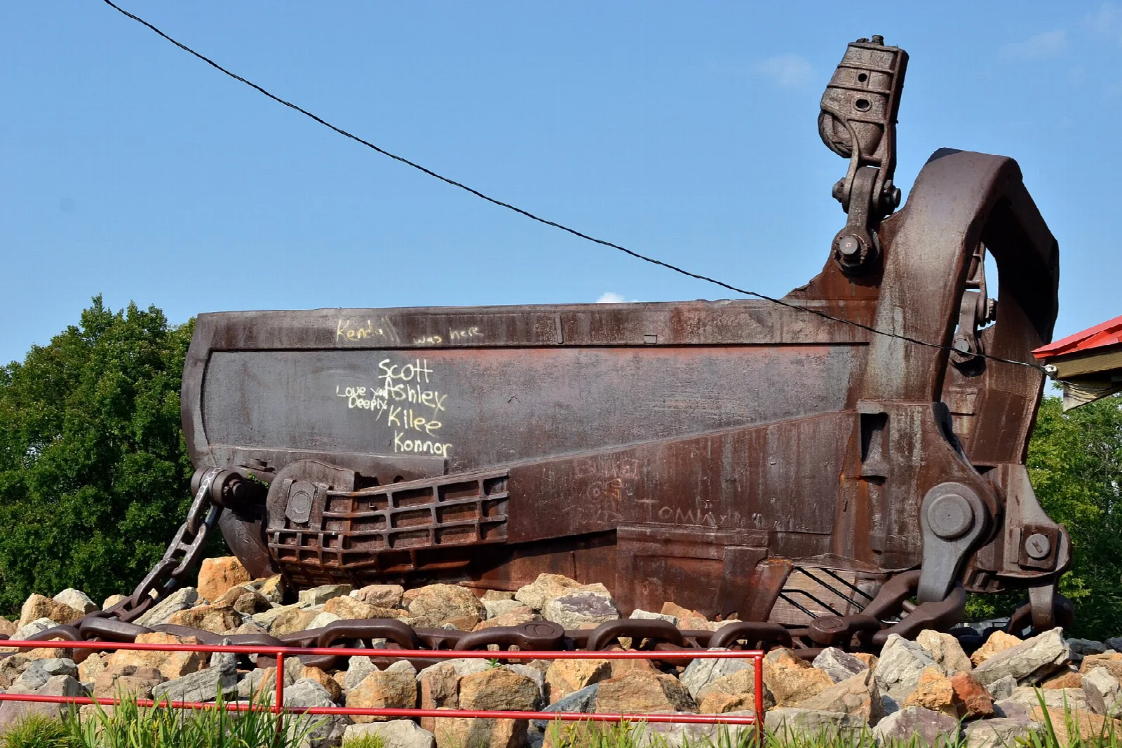 Huge rusted dragline bucket resting on a pile of rocks under a blue sky