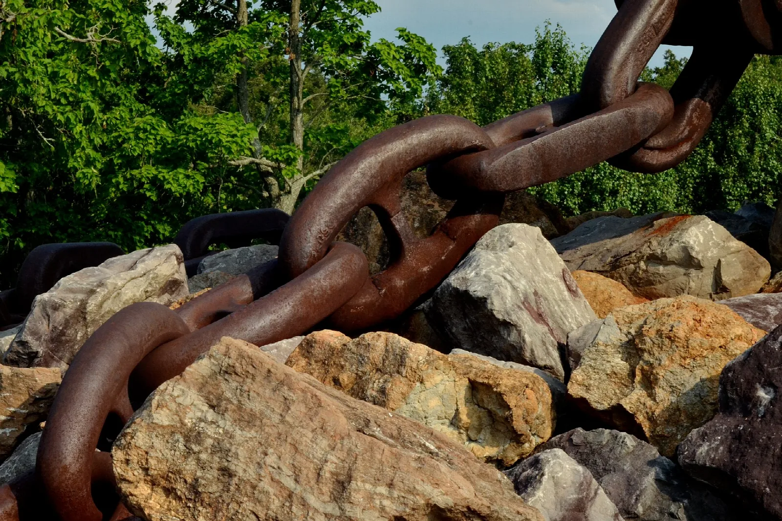 Thick rusty chain draped over large rocks with trees behind