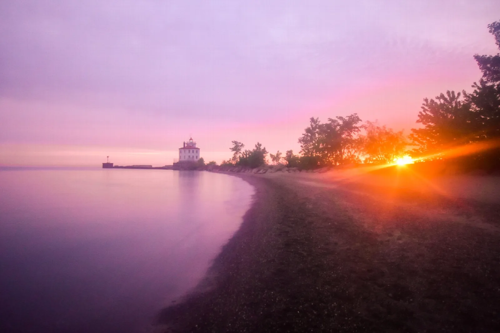 Lake shore at sunset with a purple sky and a lighthouse far down the beach