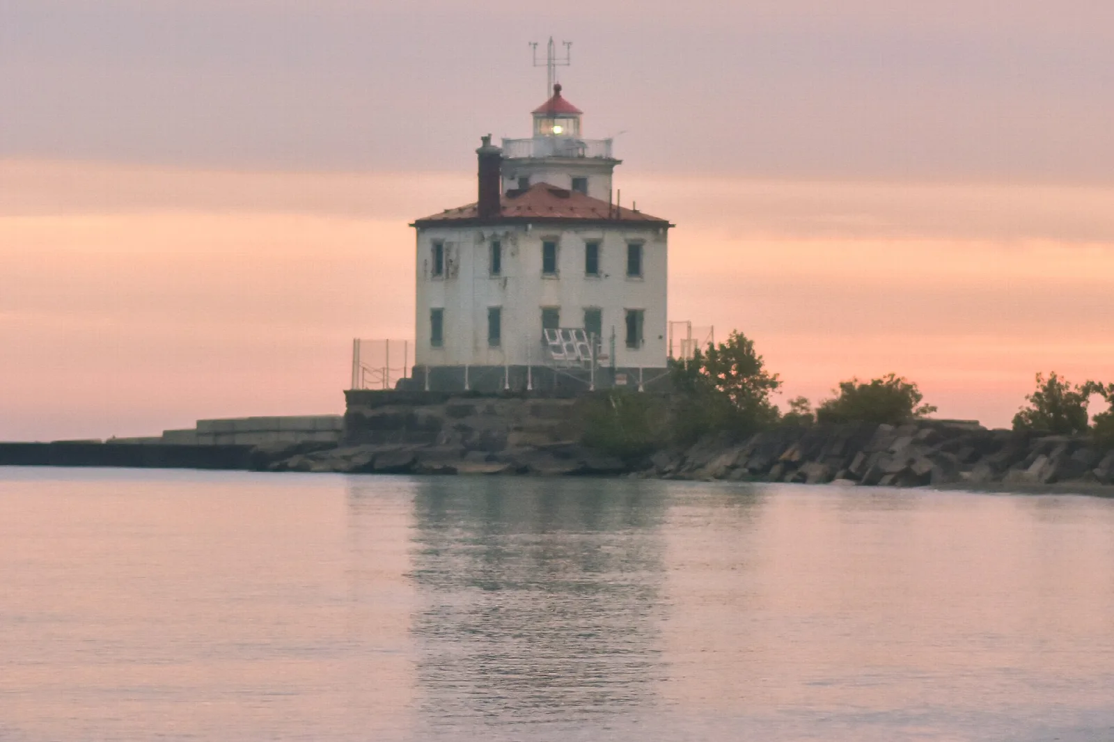 White lighthouse on a rocky breakwater at dusk with calm water